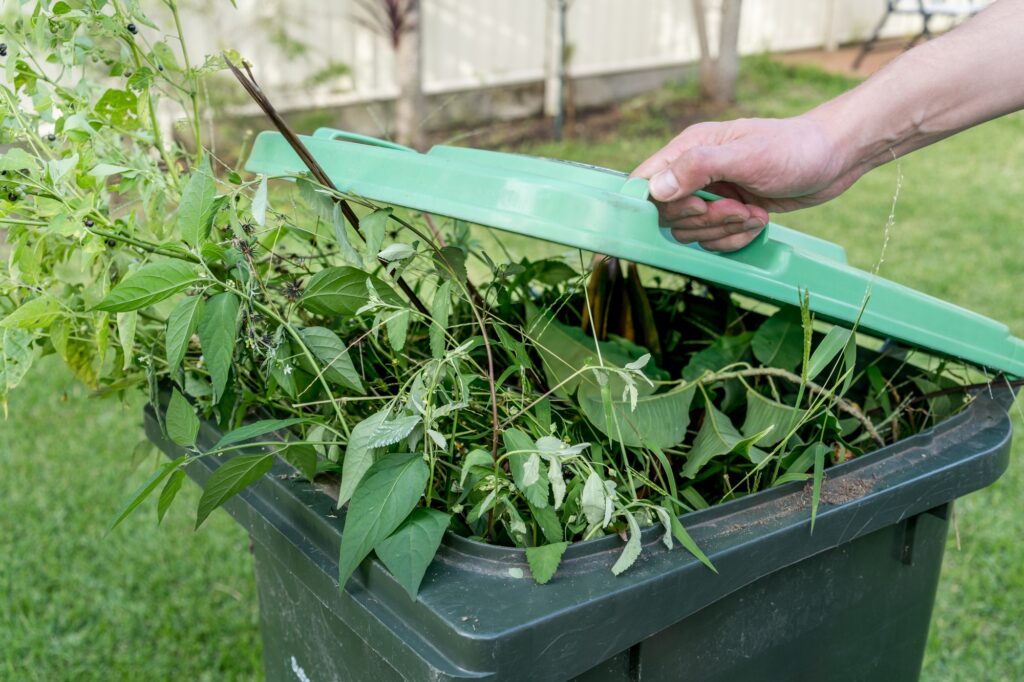 Hand closing a green rubbish garbage bin with Green garden waste. Recycling household waste