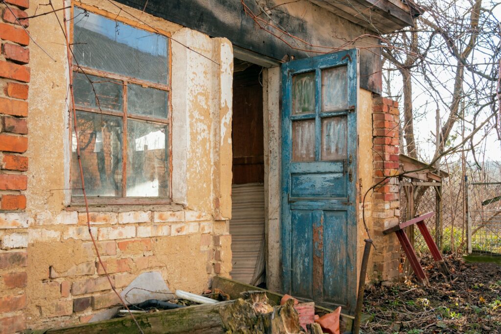 Retro-styled abandoned brick barn or farmhouse with open blue doors and big window.