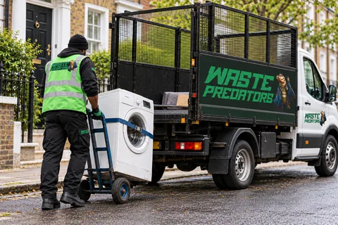 A Waste Predators worker moving a washing machine toward a mostly empty cage tipper.